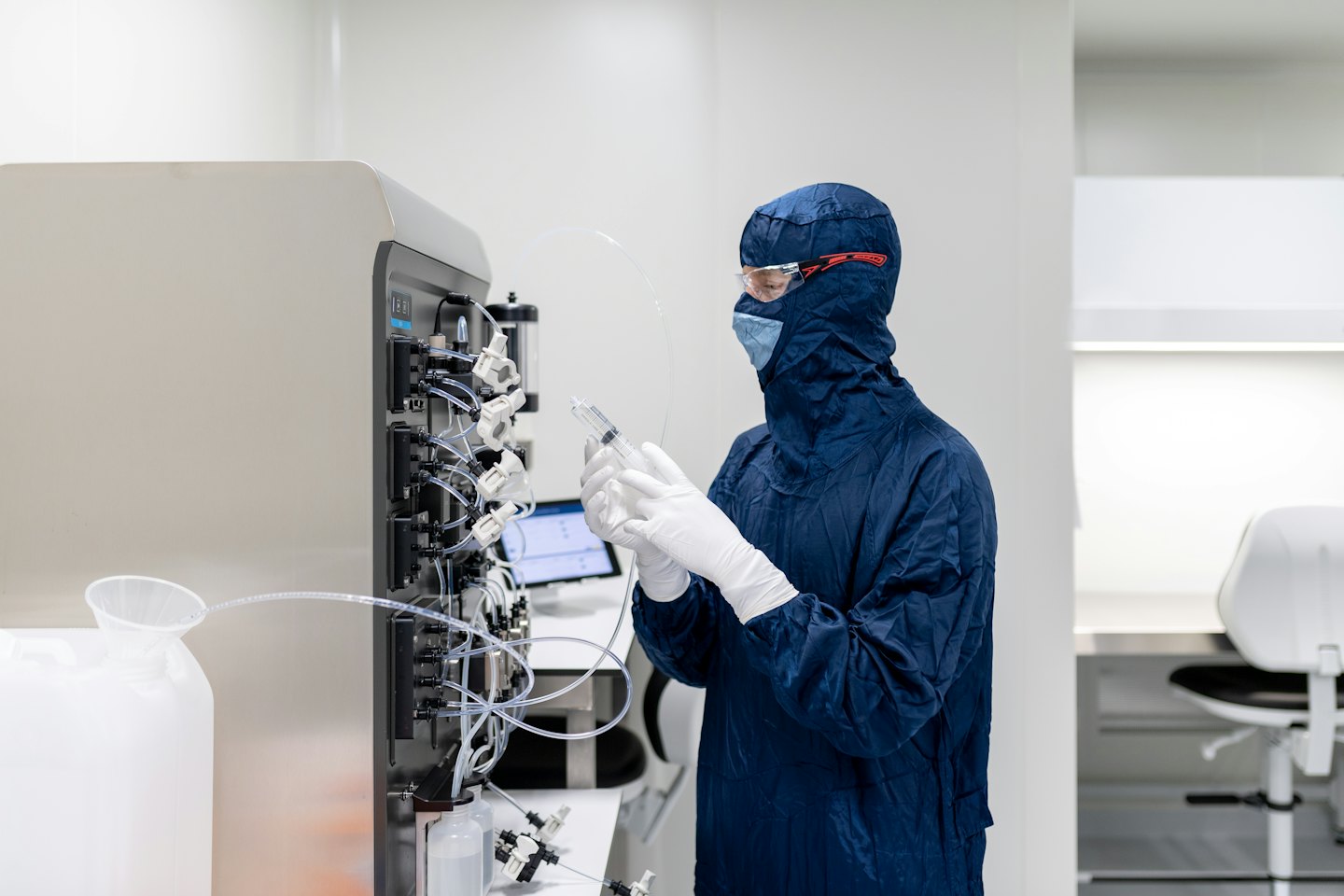 Ilmuwan berseragam cleanroom mengoperasikan mesin laboratorium kompleks dengan alat suntik.